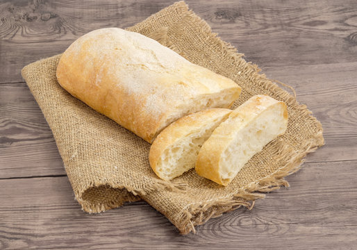 Partly sliced ciabatta on a sackcloth on wooden surface