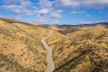 Fototapeta na wymiar Drone photograph of asphalt road leading through the dry hills of southern California canyons.