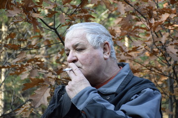 портрет курящего кавказского старика в осеннем лесу  