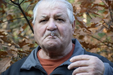 портрет курящего кавказского старика  в осеннем лесу  