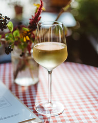 Glass of white wine on restaurant table outside with checkered tablecloth and flowers in the background