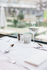 Restaurant setting, restaurant table next to window, with silver cutlery, wine glass, green outside background
