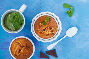 Chocolate cupkakes with mint tea in white ceramic forms on a blue background