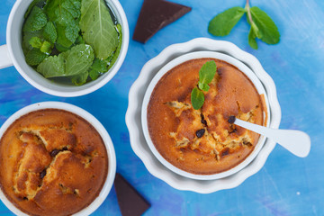 Chocolate vegan cupkakes with mint tea in white ceramic forms on a blue background