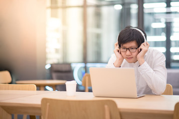 Young Asian man dressed in casual style listening to music while working with his laptop computer....
