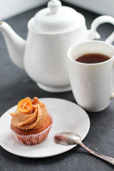 A teapot, a cup of tea and a caramel cupcake.