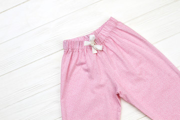 Cute pajama pants on wooden background. Elastic waistband and drawstring for snugly fit. Pink and white.