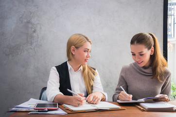 Two young european business women are sitting on the table and discussing about their work or...