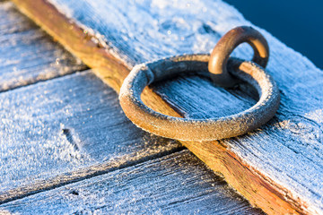 Frost covered metal mooring ring at a wooden pier on a cold morning.