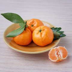 Ripe mandarins with leaves on a ceramic plate