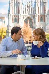 Couple of happy tourists drinking coffee on european city street in outdoors cafe, talking having fun laughing smiling happy summer holidays and dating concept in the city