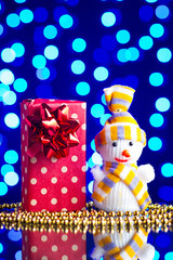Snowman toy, gift in package and golden beads on a glass table with a beautiful blue bokeh - 184251555