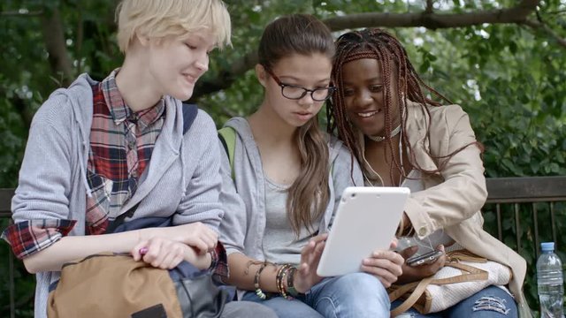 Three teen girls smiling and making faces at camera while taking selfie with digital tablet in park