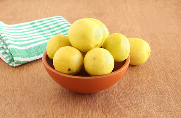 Lemons in an earthen bowl on a wooden background.