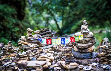 Sanskrit calligraphy of Buddhist Mantra Om Mani Padme Hum on multicolored flags hanging between two meditation stone pile on Annapurna track.