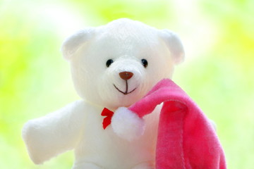Closeup one white teddy bear wear red bow with pink Christmas cap on green,yellow and white bokeh