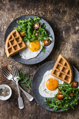 Savory waffles, fried eggs and arugula, cherry tomato salad - delicious healthy breakfast on wooden background, top view
