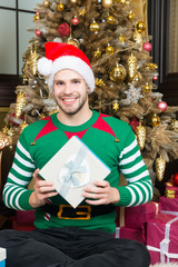 Man in santa hat smile with present at Christmas tree