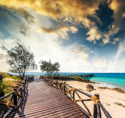 beautiful exotic landscape with wooden pier leading to the blue ocean in Africa at sunset - obrazy, fototapety, plakaty