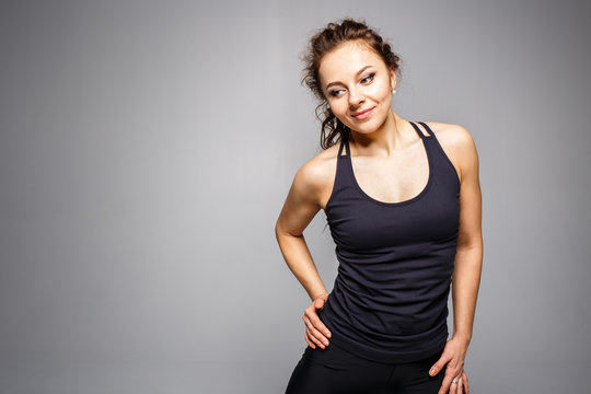 Young athletic woman standing against gray background. Fitness club concept image with copy space