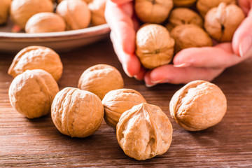 Several walnuts lie on a wooden table, in the palms of hands and in a plate