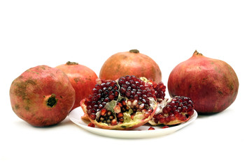 Whole and half pomegranates with ripe seeds on plate isolated on white background front view closeup