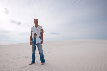 Exhausted man, lost in the desert, is standing on a sand dune