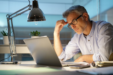 Businessman in office being thoughtful in front of laptop - obrazy, fototapety, plakaty