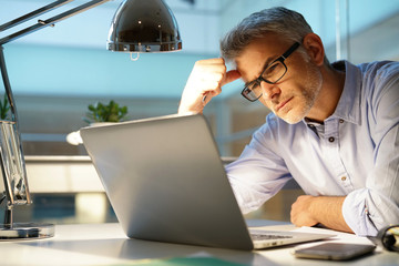 Businessman in office being thoughtful in front of laptop