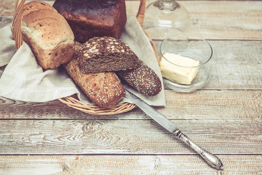 Various wheat and rye bread in a basket. Bread, table knife and butter. Healthy breakfast concept. Easy toning. Wooden background