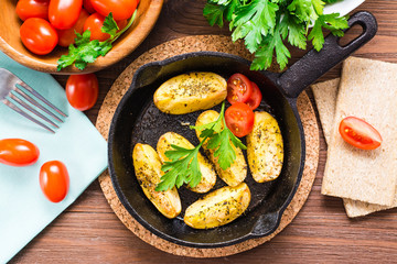 Sliced baked potatoes in an iron frying pan, cherry tomatoes and parsley leaves. Top view