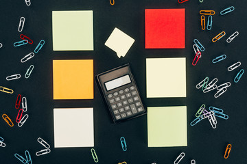 top view of calculator, colorful paper clips and blank notes on black