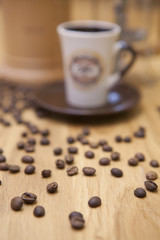 Spilled coffee beans. A cup of coffee and a background coffee maker. Shallow focus on coffee beans.
