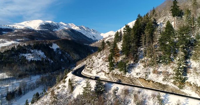 Vue a&eacute;rienne d'une voiture sur une route dangereuse dans une montagne enneig&eacute;e en hiver, sous un beau soleil - voiture route chemin roche arbre neige ciel bleu