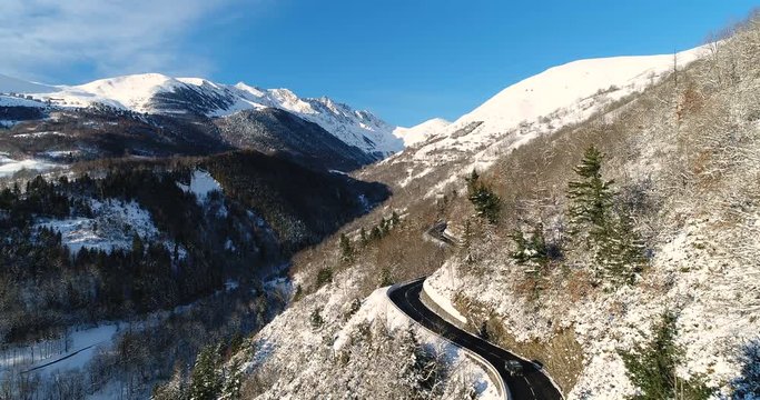 Vue a&eacute;rienne d'un 4x4 sur une route de montagne dans les Pyr&eacute;n&eacute;es en France, lors d'une journ&eacute;e ensoleill&eacute;e en hiver - voiture route chemin roche arbre neige dangereux ciel bleu