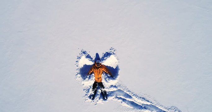 Vue rapproch&eacute;e d'un homme qui souri en r&eacute;alisant un ange allong&eacute; dans la neige - orange manteau montagne sourire bouge r&eacute;flection hiver