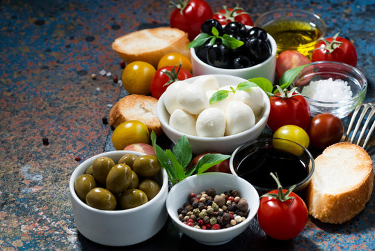 mozzarella, fresh ingredients for the salad and bread on dark background, horizontal