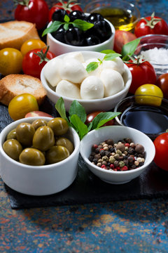 mozzarella, fresh ingredients for the salad and bread on dark background, vertical