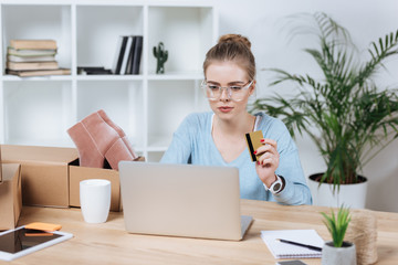 portrait of focused woman with credit card in hand looking at laptop screen at table