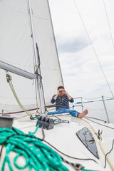 Obraz premium man sits on sailing yacht and looks through binoculars