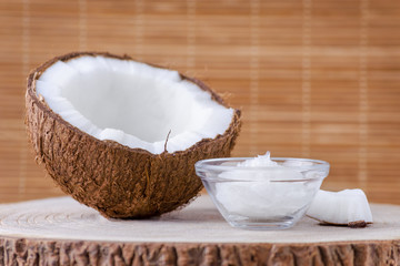 organic coconut oil in a glass bowl and coconut on natural brown background