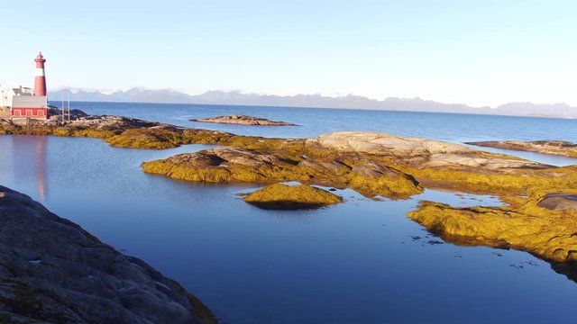 Aerial Drone moving forwards above epic nice sunny Landscape in Norway with Lighthouse and mountains in the background 4k