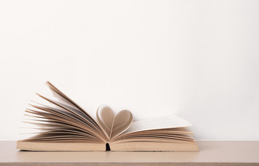 Page of book curved into heart shape on wood table. valentine concept.