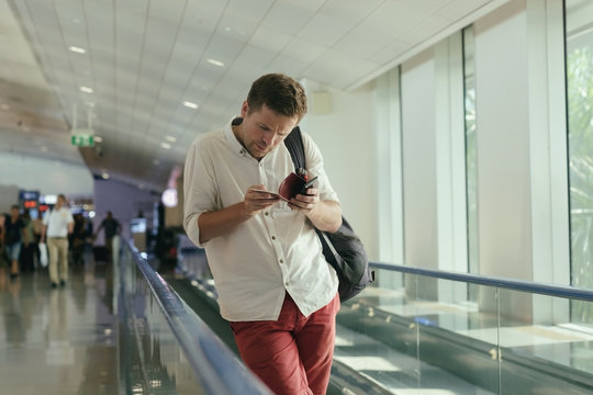 A young man in anxious looks at the tickets moving on the travolator at the airport.