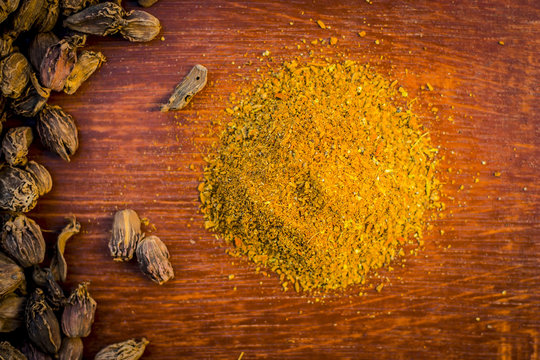 Raw black cardamom with its powder on a brownish wooden surface.