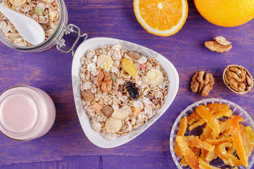 Healthy breakfast. Ceramic bowl with oat flakes, dried fruits, nuts on a violet wooden background