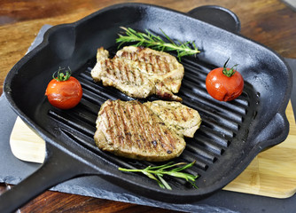 Iron pan with grill steaks, tomato and rosemary herb on a wooden table. BBQ scene