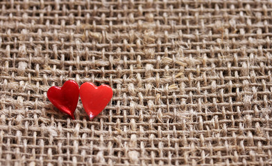 a pair of sharp pins in the form of red hearts stuck in the rough burlap