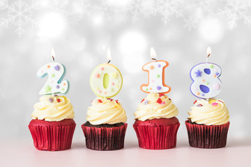 2018 Happy New Year Cupcakes with candle lit light isolated with clipping path on winter silver white glittering light and pastel pink table background