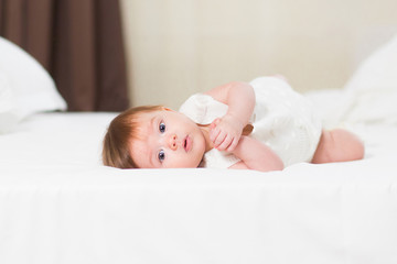 A cute 3 month baby girl in white bedding at home look nice at camera